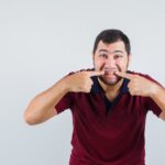Man pointing at his gums to demonstrate the early signs of receding gums and gum recession.