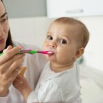 Mother brushing baby teeth with a soft toothbrush during early oral care routine